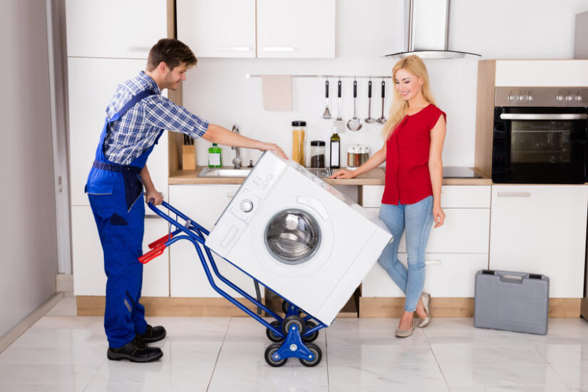 Male Worker Using Hand Truck For Carrying Washer In Kitchen