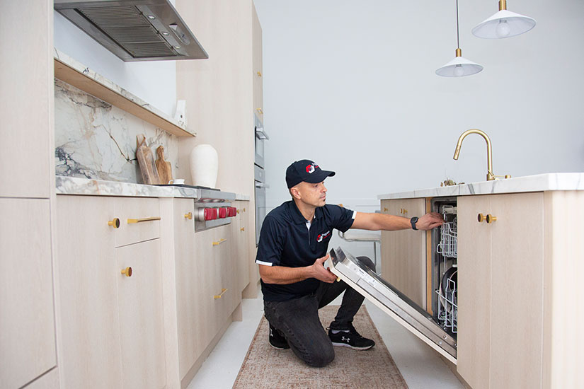 appliance repair service technician opening dishwasher in customers house